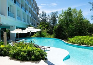 A swimming pool with lounge chairs and umbrellas, surrounded by lush greenery and a modern building. - Radisson Resort Layan Phuket (Choeng Thale)