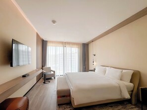 A hotel room with a large bed, a TV mounted on the wall, a desk with a chair, and a window with curtains. - Radisson Resort Layan Phuket (Choeng Thale)