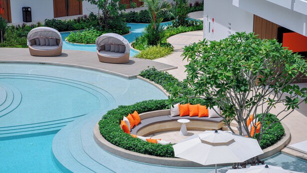 A modern pool area with a circular design, surrounded by greenery and seating areas with umbrellas. - Radisson Resort Layan Phuket (Choeng Thale)