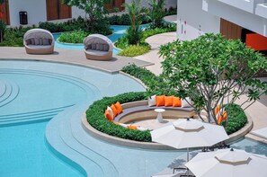 A modern pool area with a circular design, surrounded by greenery and seating areas with umbrellas. - Radisson Resort Layan Phuket (Choeng Thale)