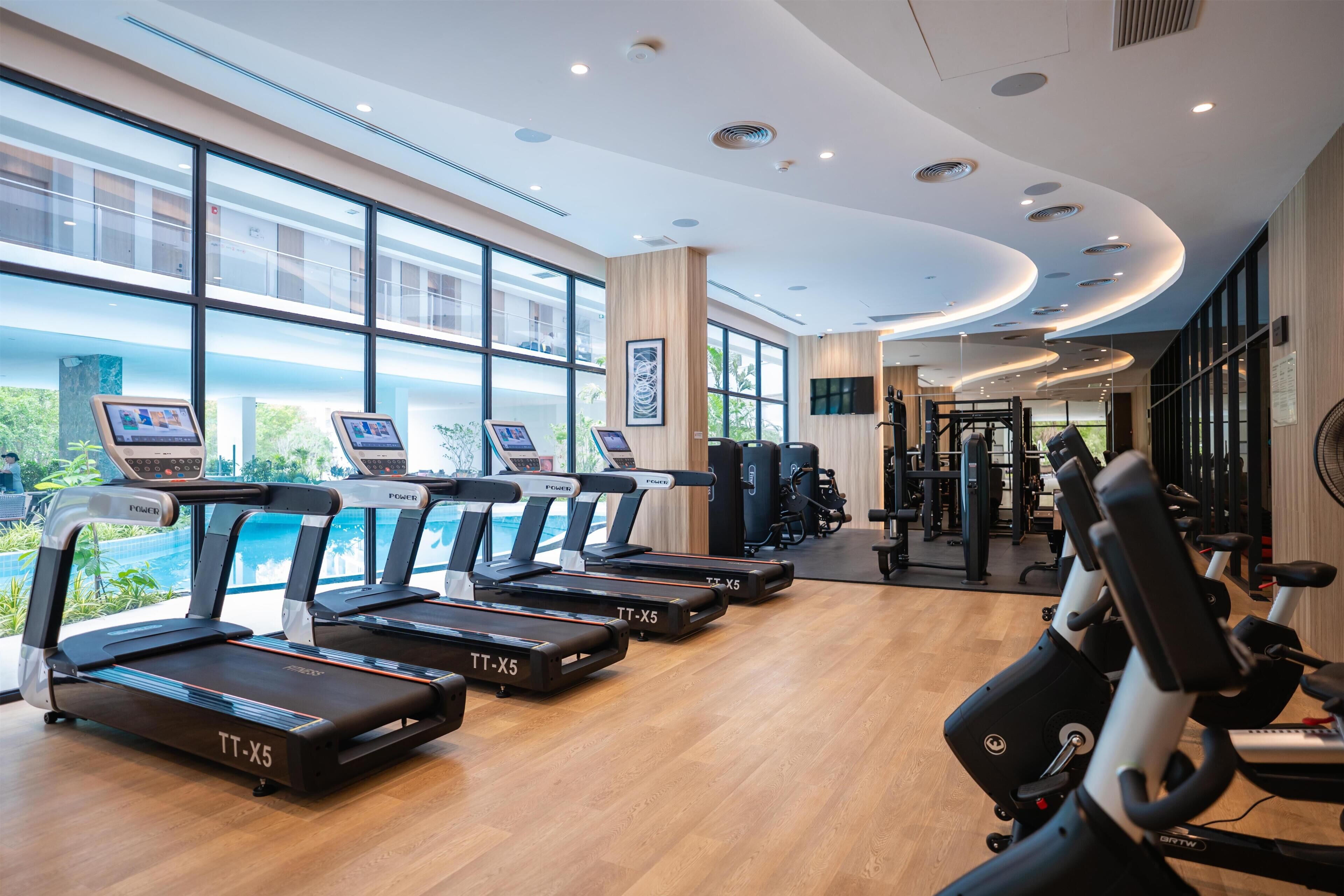 A gym with multiple treadmills, exercise equipment, and large windows offering views of the outdoors.