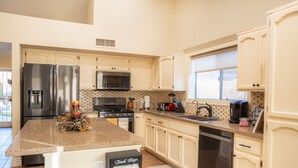 A modern kitchen with a stainless steel refrigerator, a microwave, a stove, and a dishwasher. There is a large island with a trash bin and a vase of flowers. - Game Room/ Pool  Cozy Home in Yuma (Yuma)