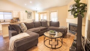A living room with a sectional sofa, a glass coffee table, a fireplace, and a ceiling fan. - Game Room/ Pool  Cozy Home in Yuma (Yuma)
