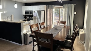 A modern kitchen with white cabinets, a dining table with chairs, and a large window with curtains. - Seabright Sanctuary - COMFY beds - mins from Margaritaville! (Osage Beach)