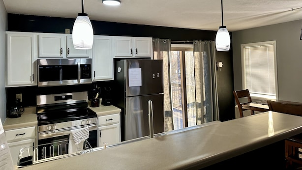 A modern kitchen with white cabinets, stainless steel appliances, pendant lights, and a view of the outdoors through a window. - Seabright Sanctuary - COMFY beds - mins from Margaritaville! (Osage Beach)