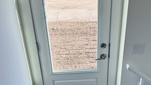 Una porta bianca con una finestra, un tappetino d'ingresso nero e un interruttore a muro.