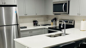 Una cucina moderna con mobili grigi, elettrodomestici in acciaio inossidabile, un'isola centrale con sgabelli da bar e un forno a microonde sopra il lavello.