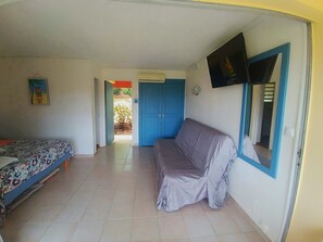 A room with a bed, a couch, a TV mounted on the wall, and a door leading to another room. - Studio RDC 22m2 + 13m2 Terrasse 1 à 4 Personnes / Proche mer Ste Anne Martinique (Sainte-Anne)