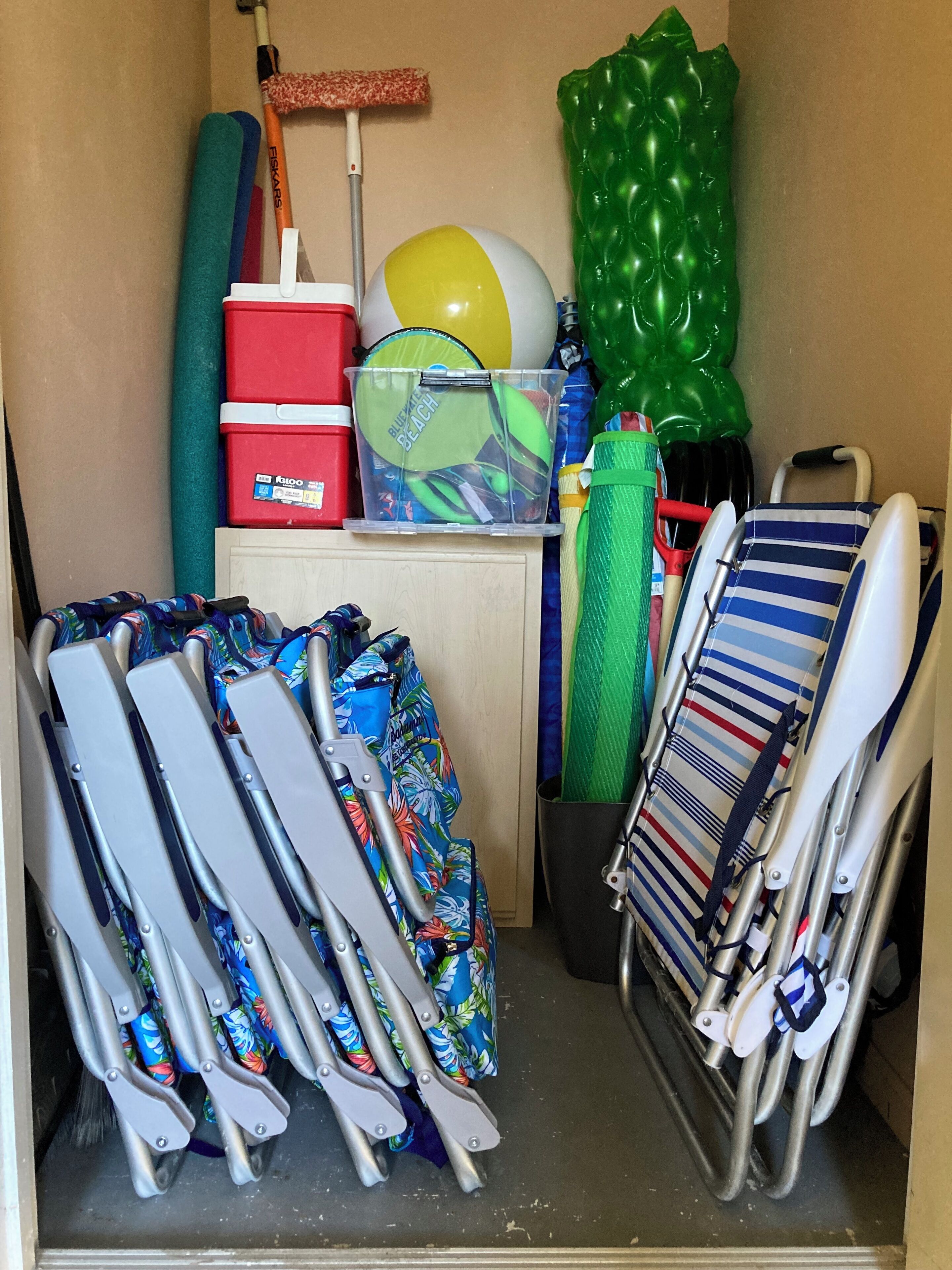 A storage area with folding chairs, a beach ball, a mop, and various containers.
