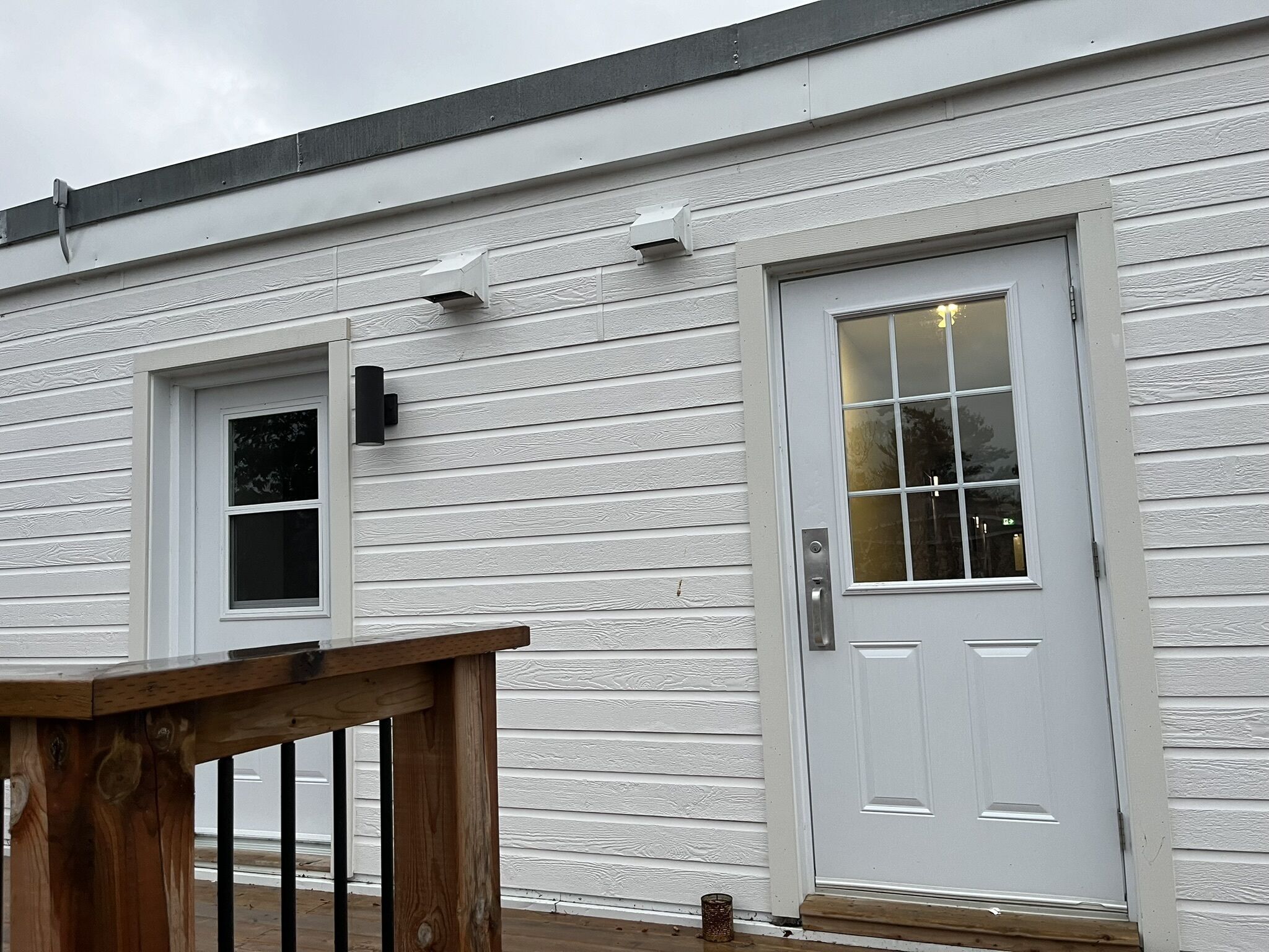 A white building with a front door, a small window, and a wooden railing.