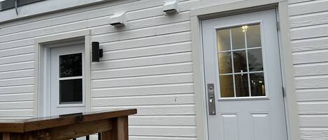 A white building with a front door, a small window, and a wooden railing.