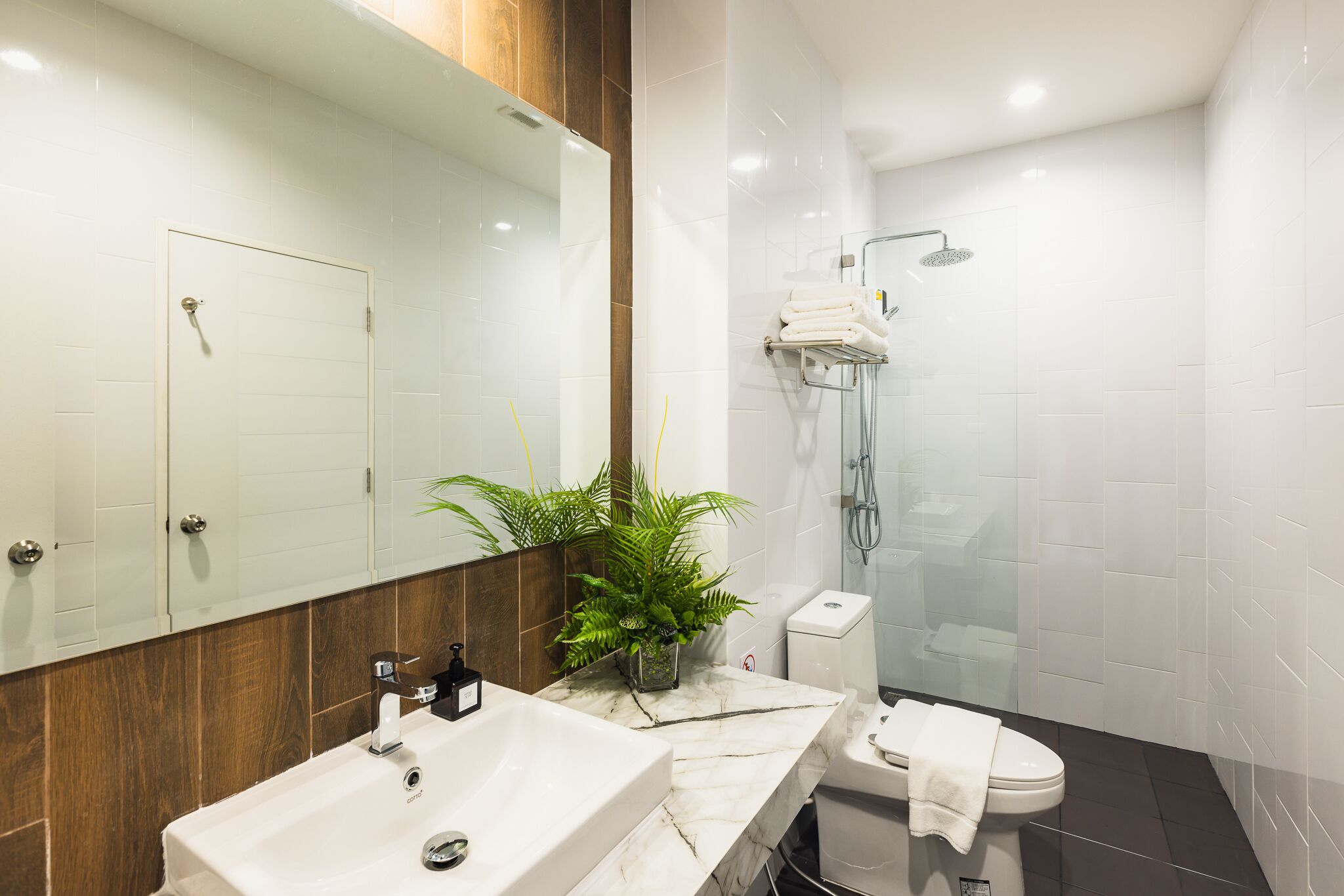A modern bathroom with a large mirror, a marble sink, a toilet, and a shower area.