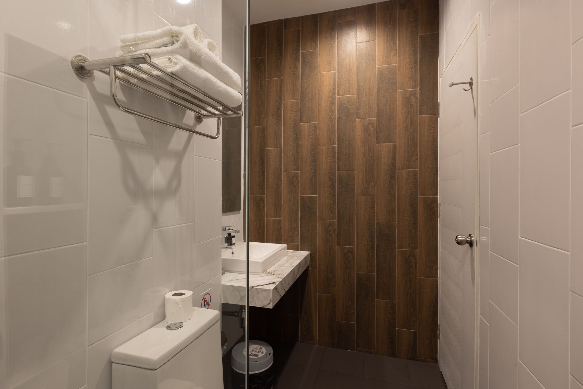 Une salle de bain moderne avec une douche à parois de verre, des accessoires blancs et un mur d’accent en bois.