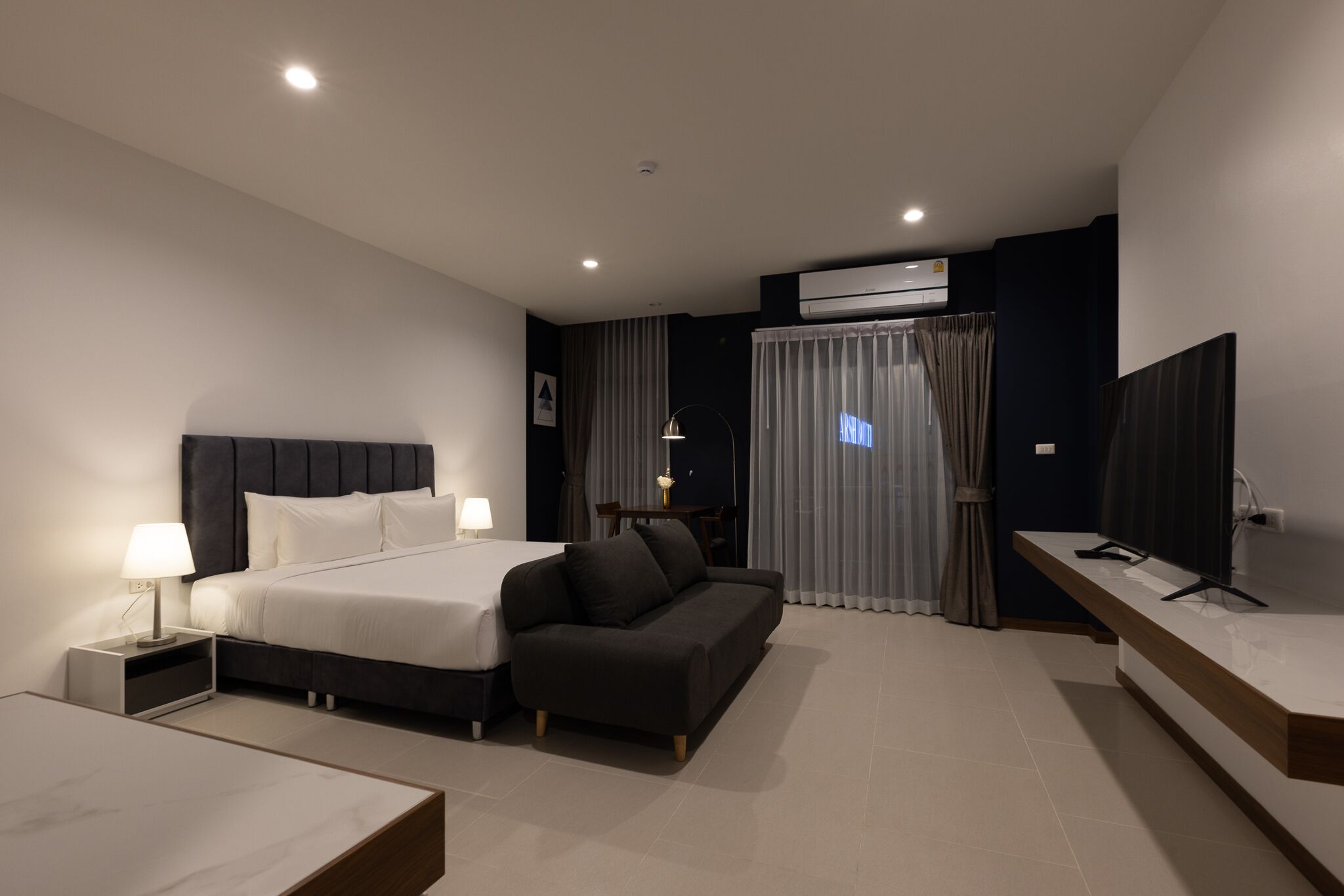 Ein modernes Hotelzimmer mit einem großen Bett, einer Couch, einem Schreibtisch und einem Fernseher.