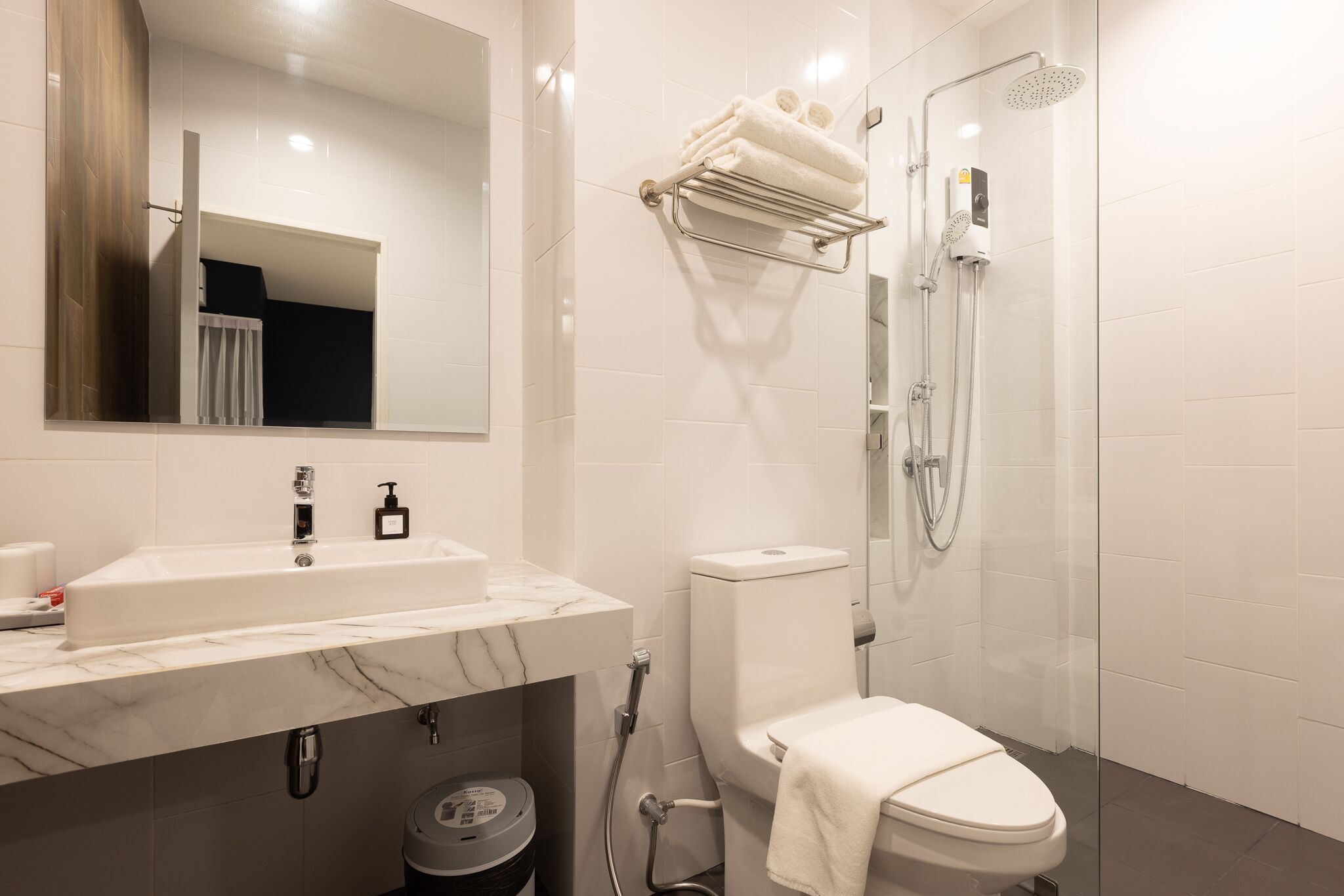 A modern bathroom with a marble sink, a toilet, a glass shower enclosure, and a towel rack.
