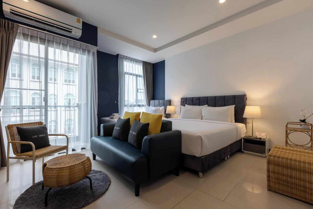 A modern hotel room with a large bed, a sofa, a chair, and a small table.