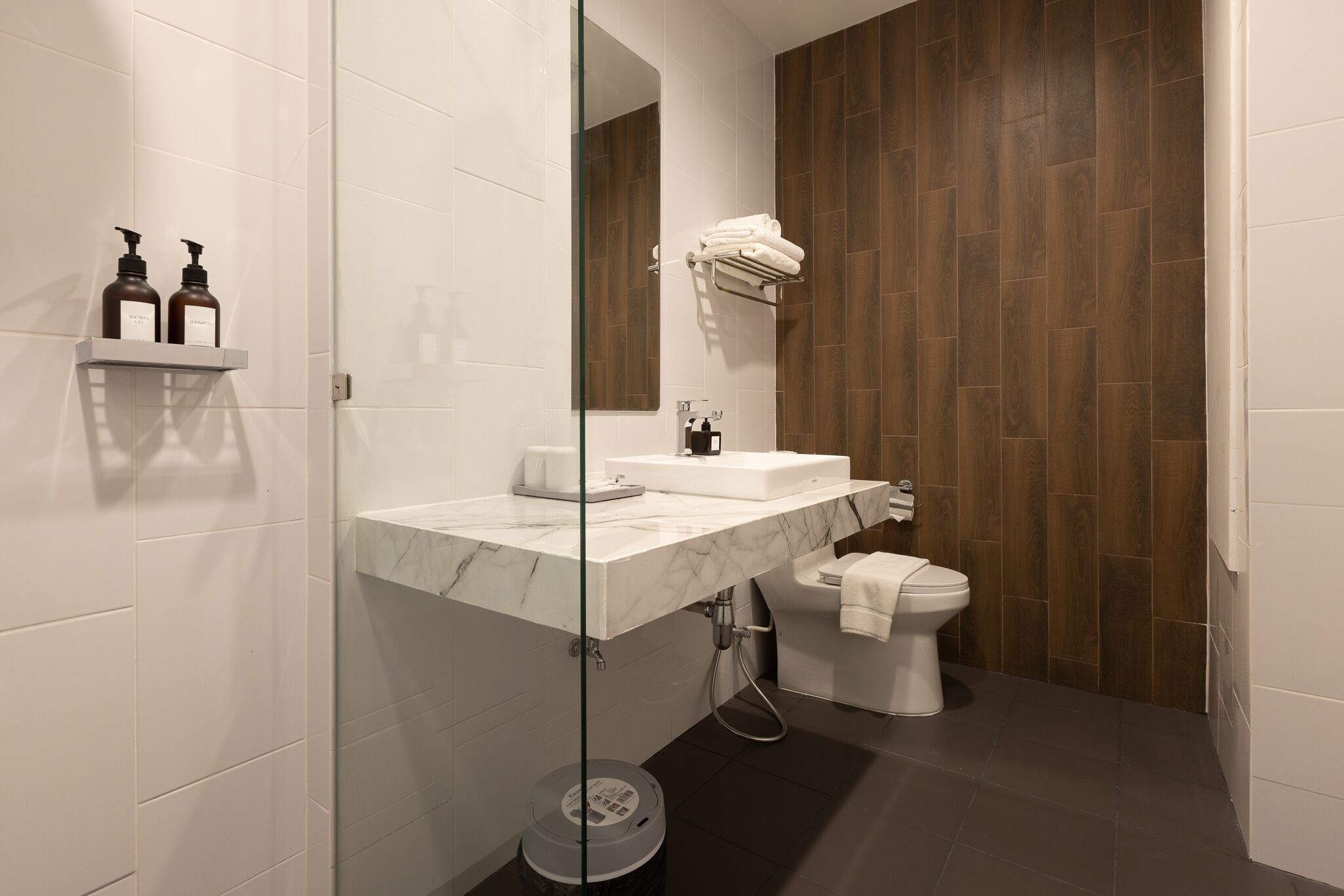 Ein modernes Badezimmer mit Marmorplatte, einer Duschkabine aus Glas, einer weißen Toilette und Holzpaneelen.