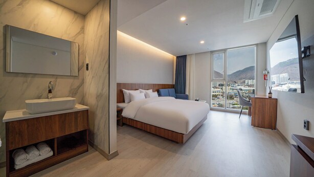 A modern hotel room with a large bed, a built-in vanity with a sink, a large window offering a city view, and a flat-screen TV mounted on the wall. - Orayeon Hotel Yeongwol (Yeongwol)