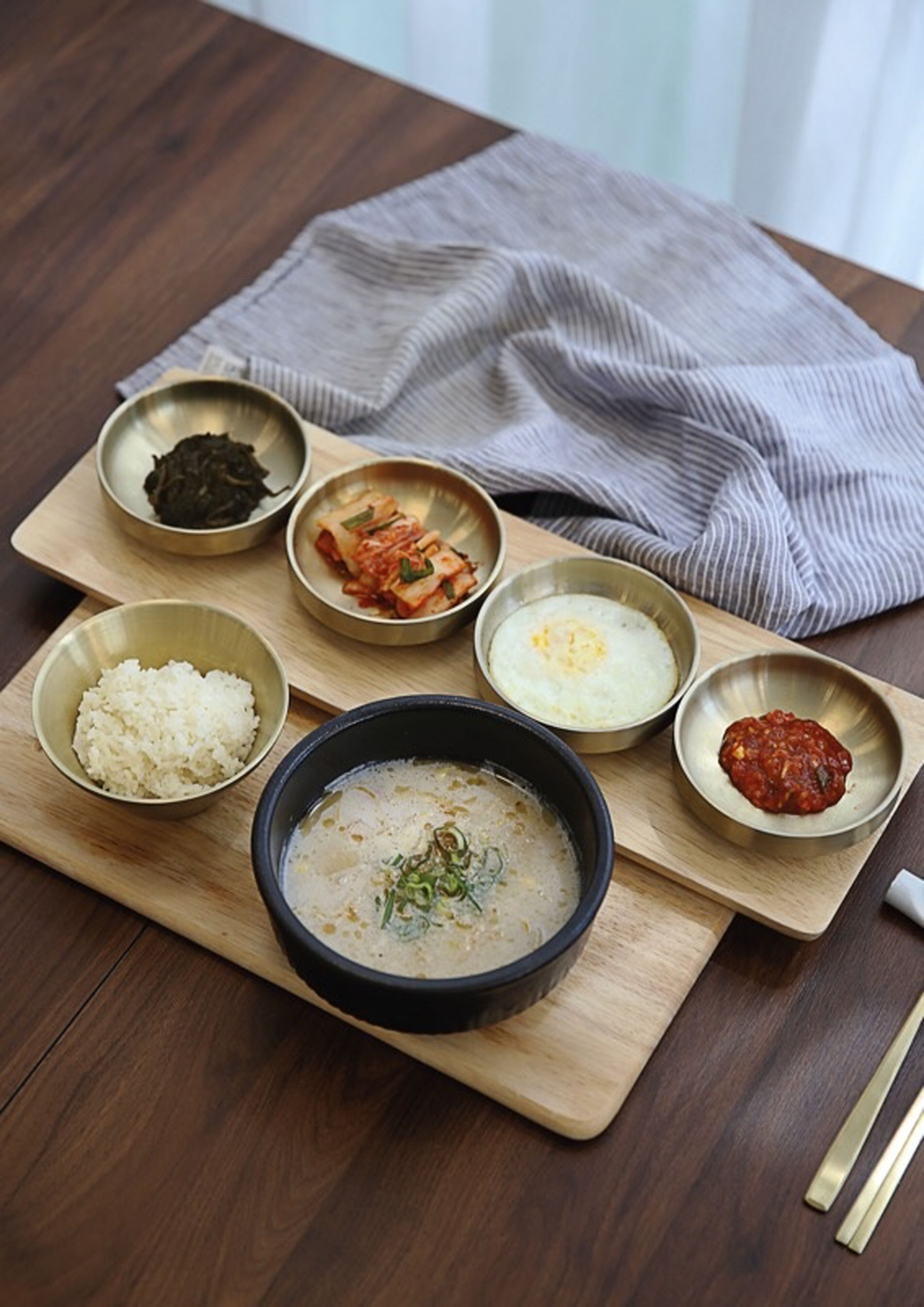 Un pasto con riso, zuppa e diversi contorni su un tagliere di legno.
