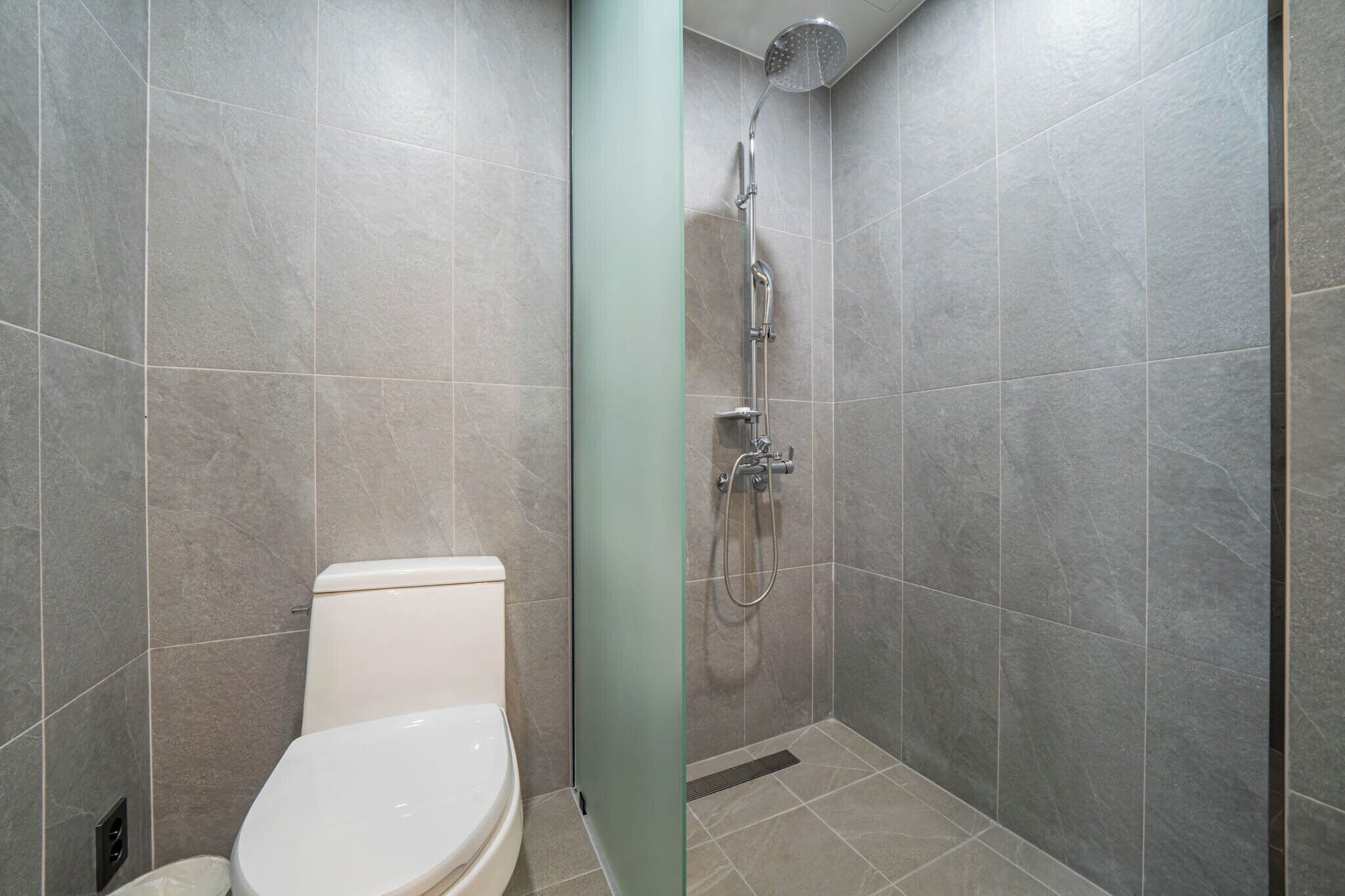 A modern bathroom with a shower, toilet, and a glass partition.