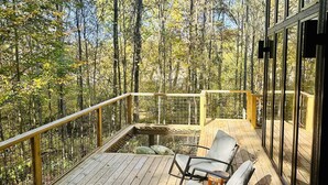A wooden deck with two lounge chairs and a glass railing overlooking a forest. - Anjuna River House - the hidden Scandi cabin on 12 acres in Southern Indiana!  (New Pekin)