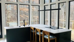 A modern kitchen with large windows, a central island, and bar stools. - Anjuna River House - the hidden Scandi cabin on 12 acres in Southern Indiana!  (New Pekin)