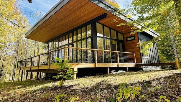 A modern wooden cabin with large windows and a deck, surrounded by autumn trees. - Anjuna River House - the hidden Scandi cabin on 12 acres in Southern Indiana!  (New Pekin)