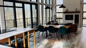 A modern kitchen with large windows, a dining area with a wooden table and chairs, and a kitchen island. - Anjuna River House - the hidden Scandi cabin on 12 acres in Southern Indiana!  (New Pekin)
