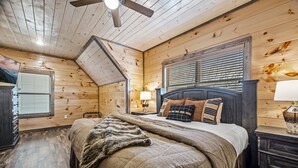 Et hyggeligt soveværelse med træloft, en seng med mange puder, et natbord og en lampe.