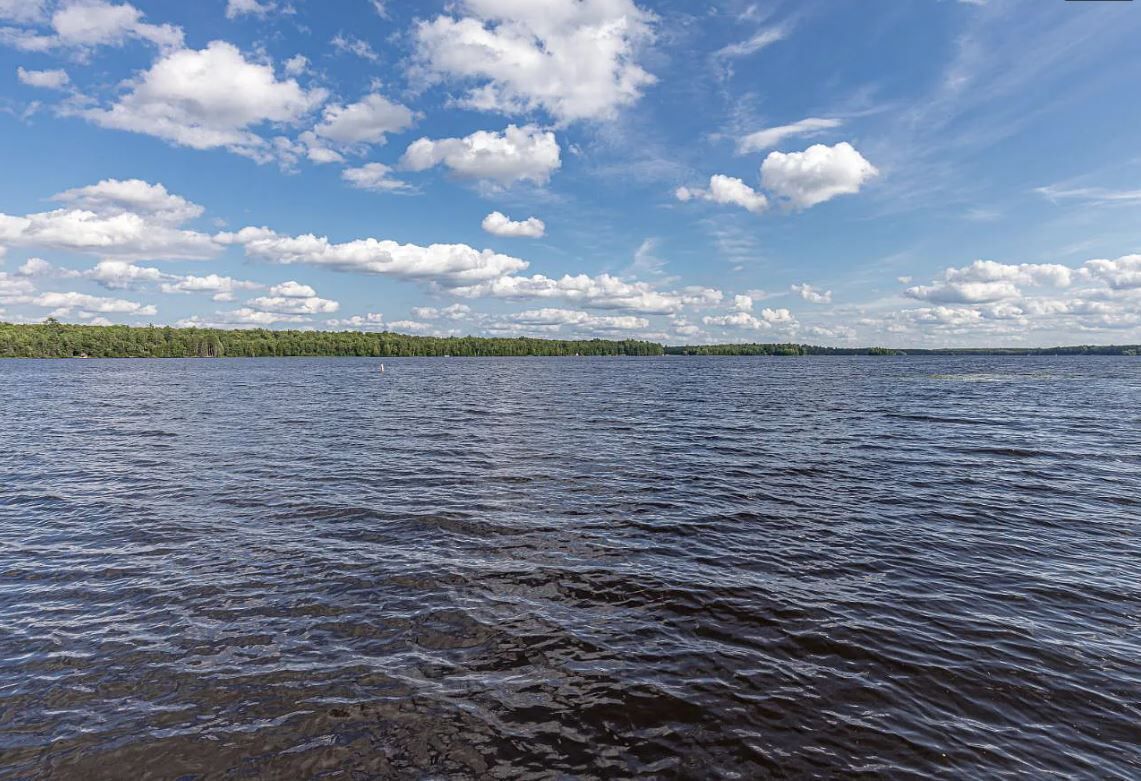 A calm lake with a forested shoreline under a partly cloudy sky.
