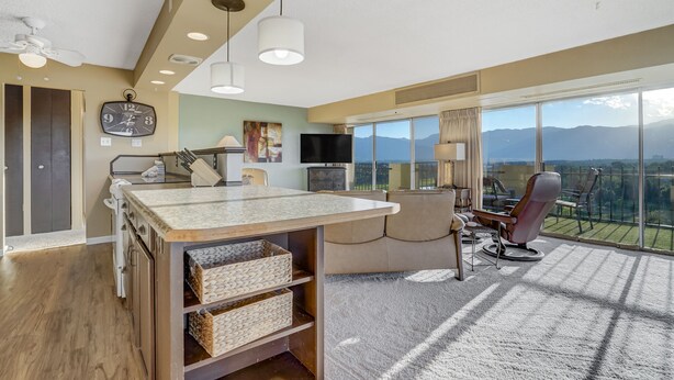 Une chambre d’hôtel moderne dotée d’une grande fenêtre, d’un téléviseur à écran plat, d’un coin repas avec un comptoir de cuisine et d’un espace salon confortable offrant une vue sur les montagnes.