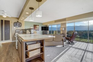 Une chambre d’hôtel moderne dotée d’une grande fenêtre, d’un téléviseur à écran plat, d’un coin repas avec un comptoir de cuisine et d’un espace salon confortable offrant une vue sur les montagnes.