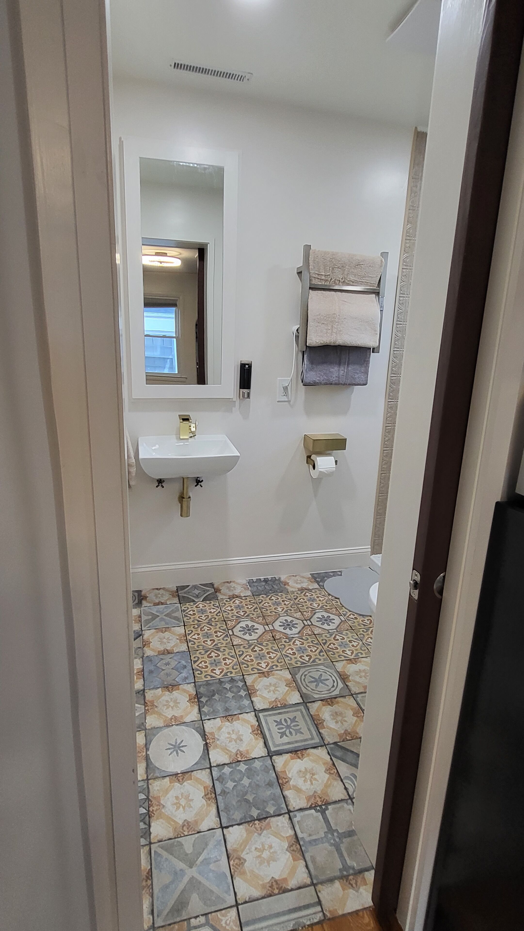 Ein Badezimmer mit gefliestem Boden, einem Waschbecken, einem Spiegel und einem Handtuchhalter.