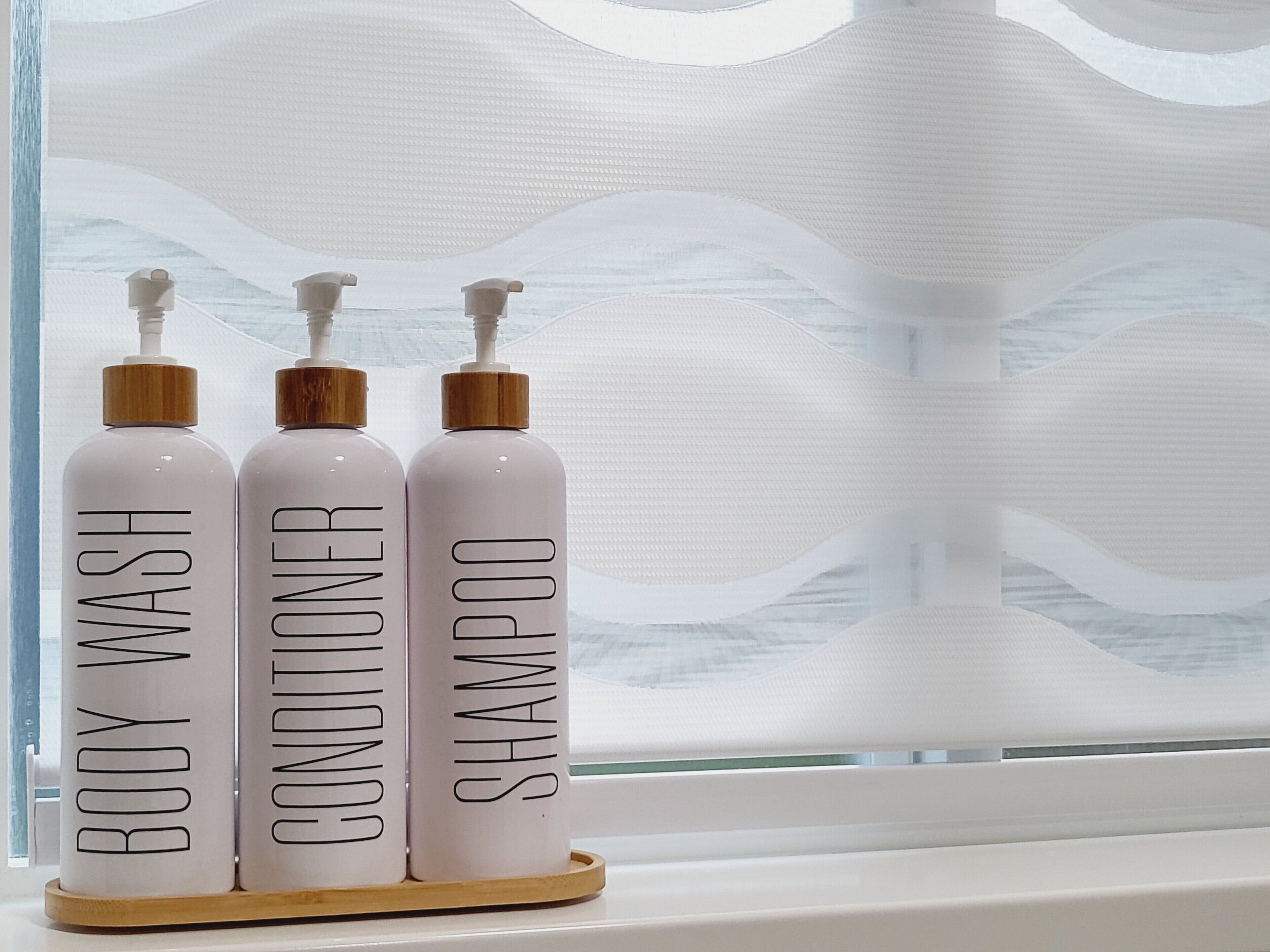 Three bottles of body wash, conditioner, and shampoo on a wooden tray.