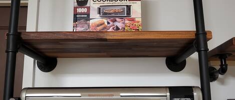 Une friteuse à air numérique est posée sur une étagère, et un livre de recettes intitulé « Ninja Foodi Digital Air Fry Oven 2021 » se trouve juste au-dessus.