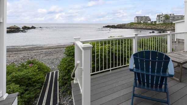 A wooden deck with a blue chair, overlooking a rocky shoreline and a calm sea.