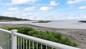 A beach with a rocky shoreline, a white railing, and green vegetation.
