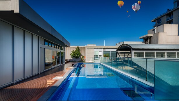 Una piscina moderna en la azotea con barandillas de cristal y terraza de madera.