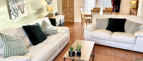 A living room with two white leather sofas, a coffee table, and a dining area with a wooden table and chairs.