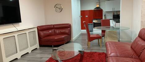 Ein modernes Wohnzimmer mit einem roten Ledersofa, einem Glastisch und einem Fernseher auf einem weißen Schrank.