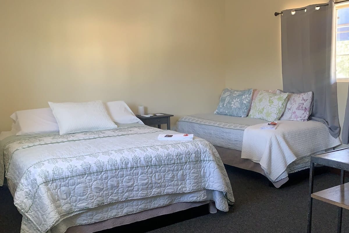 A hotel room with two beds, a small table, and a window with curtains.