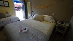 A hotel room with two beds, a small bedside table with a lamp, and a view of the street outside. - VILLA BRASIL MOTEL (Los Angeles)