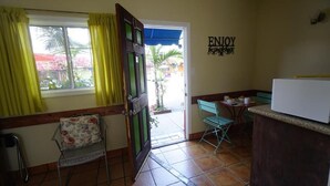A small kitchen with a window, a door, a chair, a table, and a wall sign. - VILLA BRASIL MOTEL (Los Angeles)
