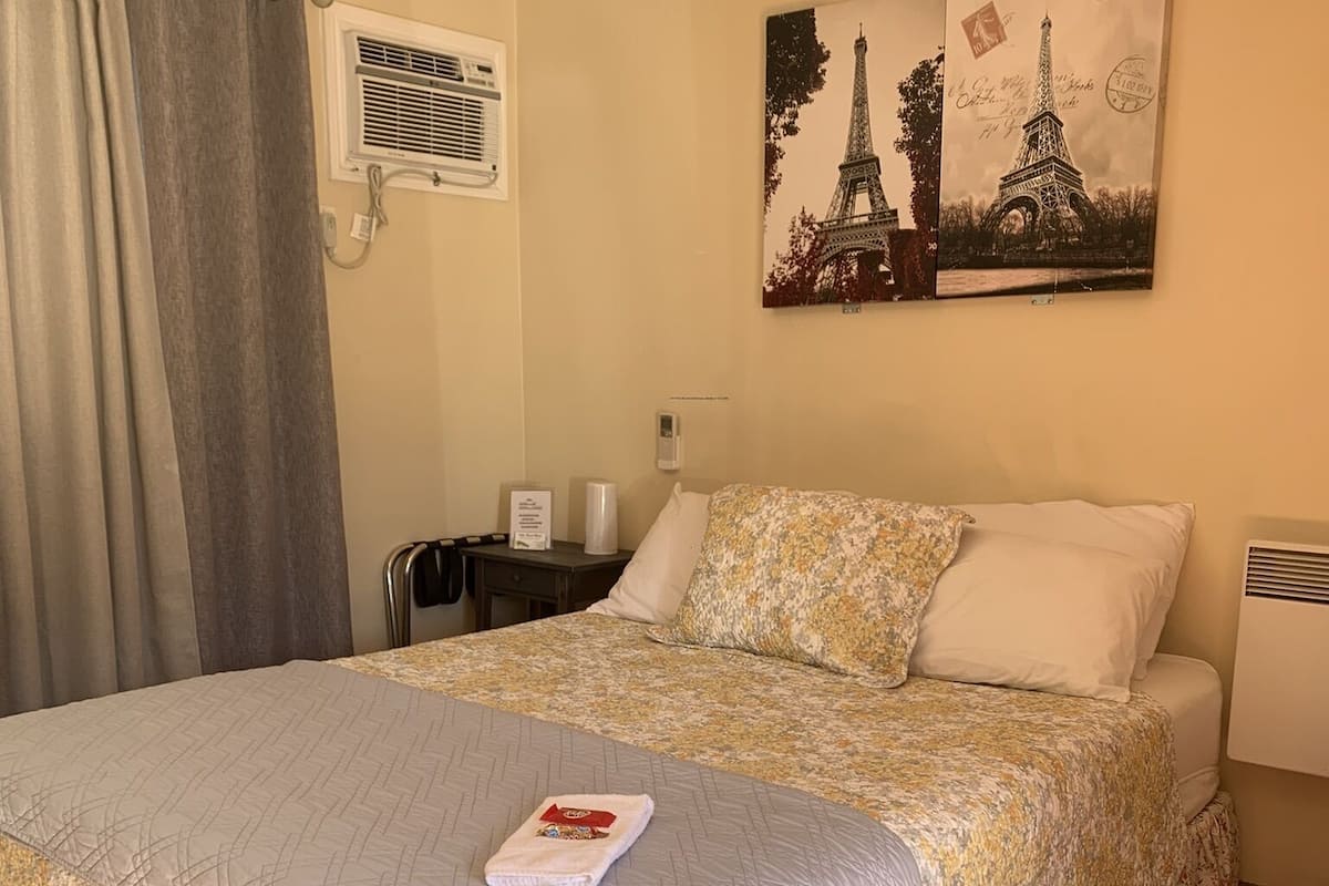 A neatly made bed with a floral bedspread, a wall-mounted picture of the Eiffel Tower, and a window with a curtain.