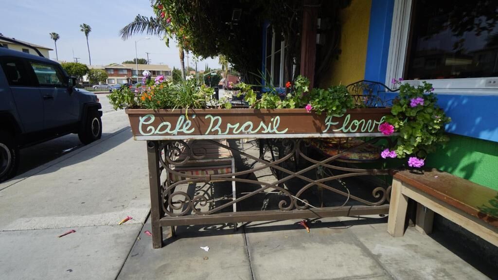Ein Metallgitter mit einem Schild, auf dem 'Cafe Brasil Flowers' steht, und mit Kübelpflanzen.