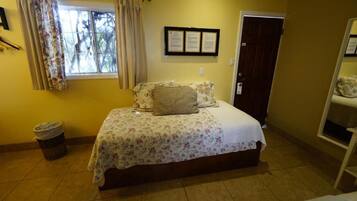 A bedroom with a bed, a window with curtains, a door, and a wall-mounted certificate.