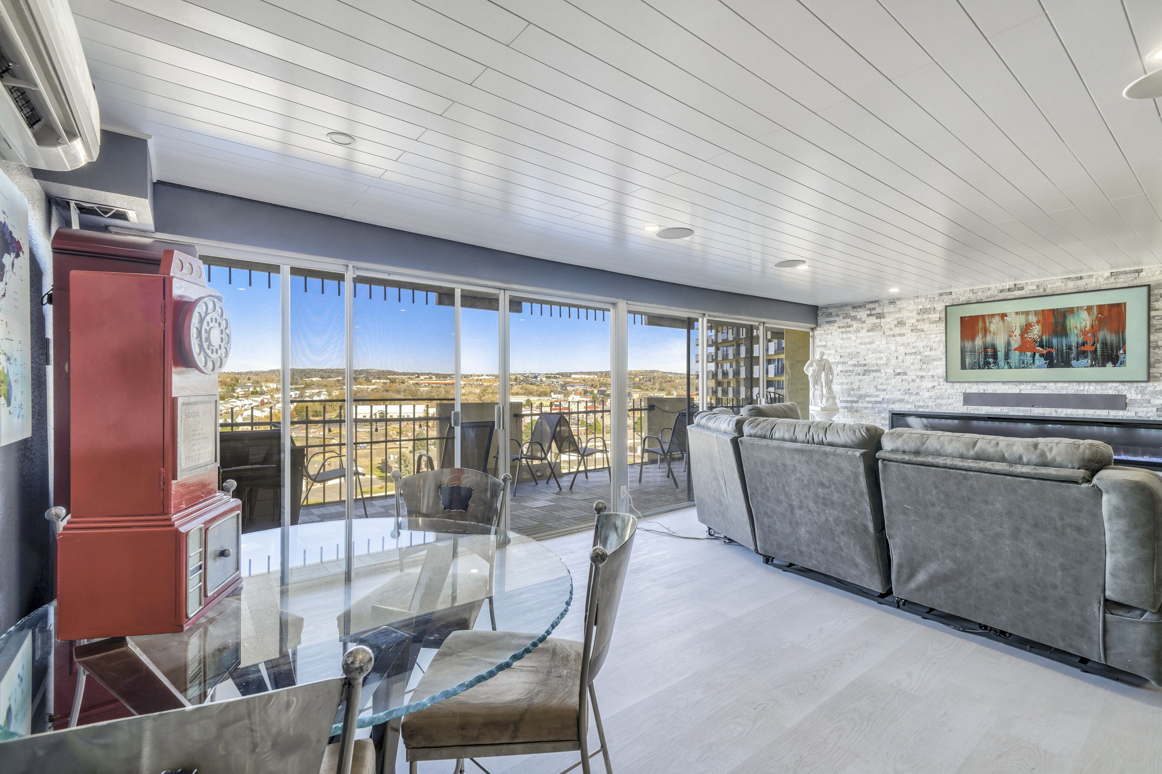 Un balcon spacieux offrant une vue dégagée sur le paysage urbain, un salon moderne avec un canapé et une table en verre, et un téléphone vintage rouge.