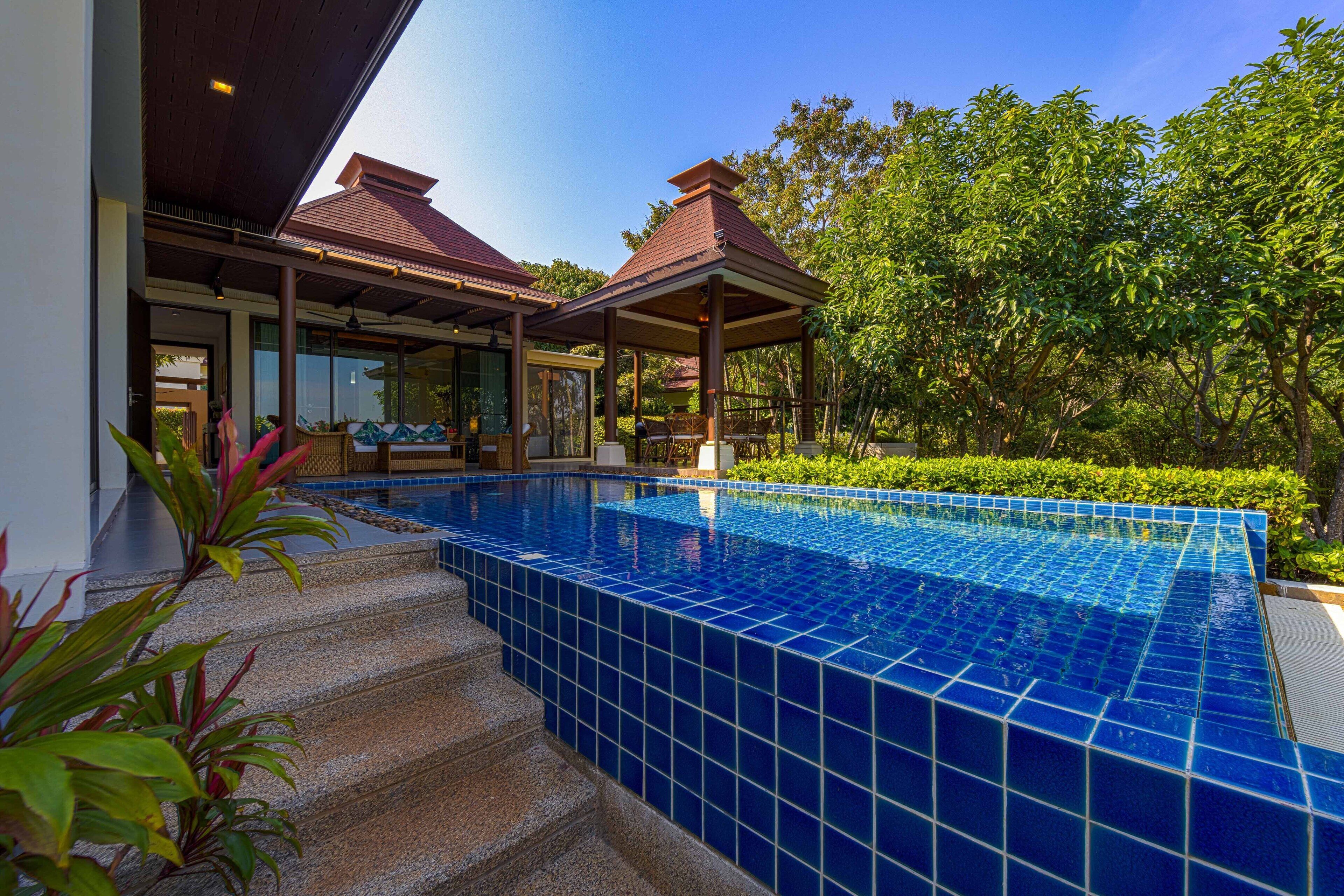Una piscina con azulejos azules, rodeada de escalones y vegetación.