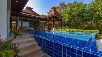Una piscina con azulejos azules, rodeada de escalones y vegetación.