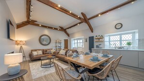 Eine geräumige Küche mit Holztisch gedeckt für ein Essen, ein Essbereich mit einer Couch und einer Küchenarbeitsplatte mit Spüle und Fenster.